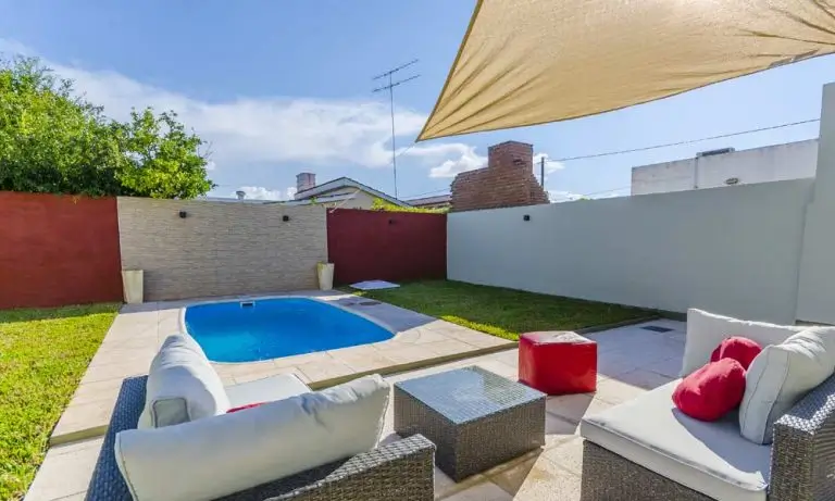 Pileta de fibra de vidrio Moldear Línea Banco y Escalera (modelos MBE490 y MBE590) instalada en un patio con living exterior y vela de sombra